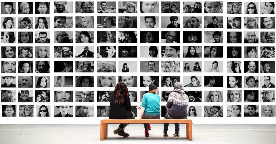 People sitting on a bench in front of wall covered in black and white pictures of people