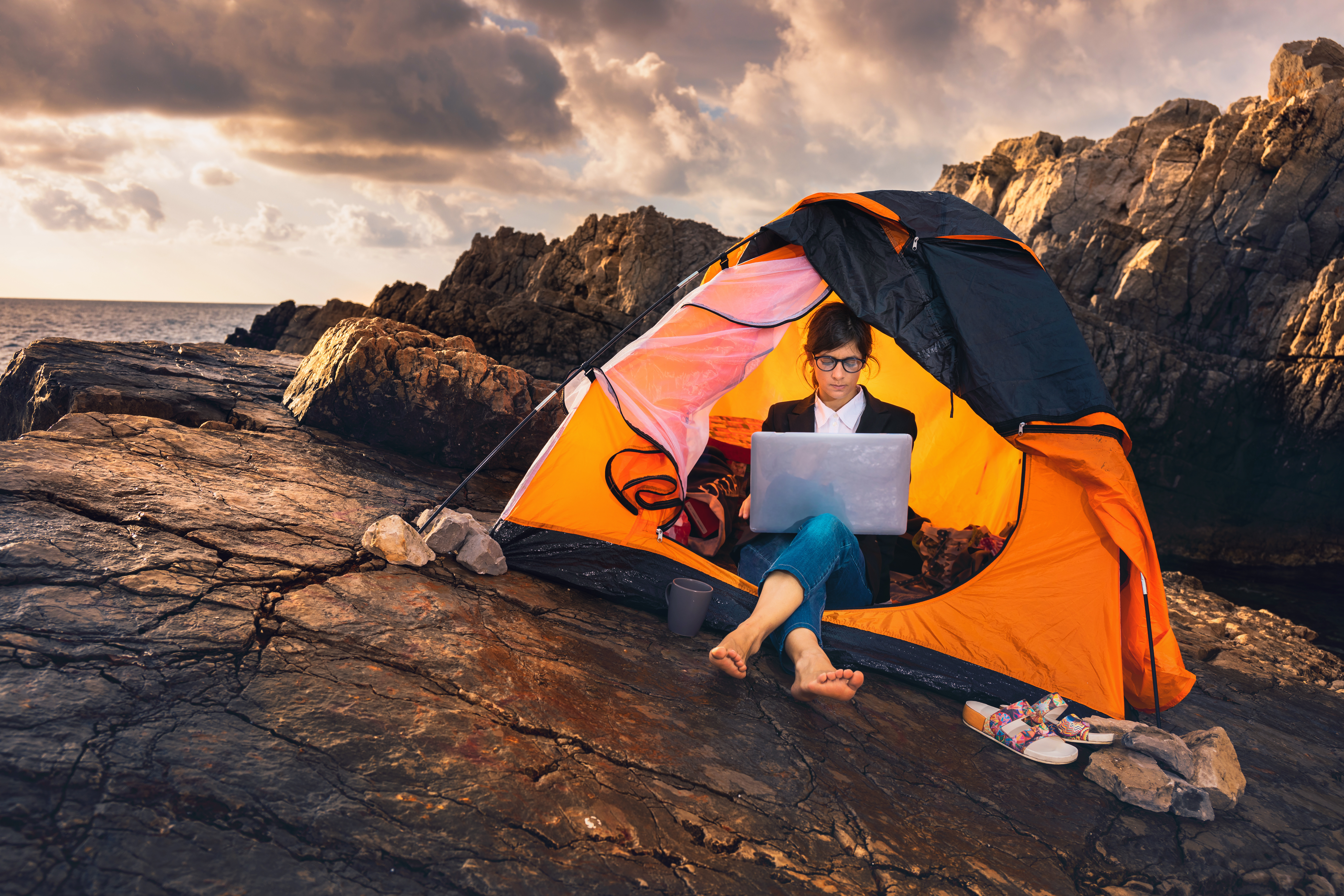 Women working on a laptop sitting in a small tent on the side of a cliff