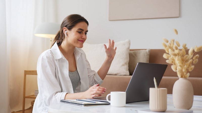 Woman working at home waving on video call